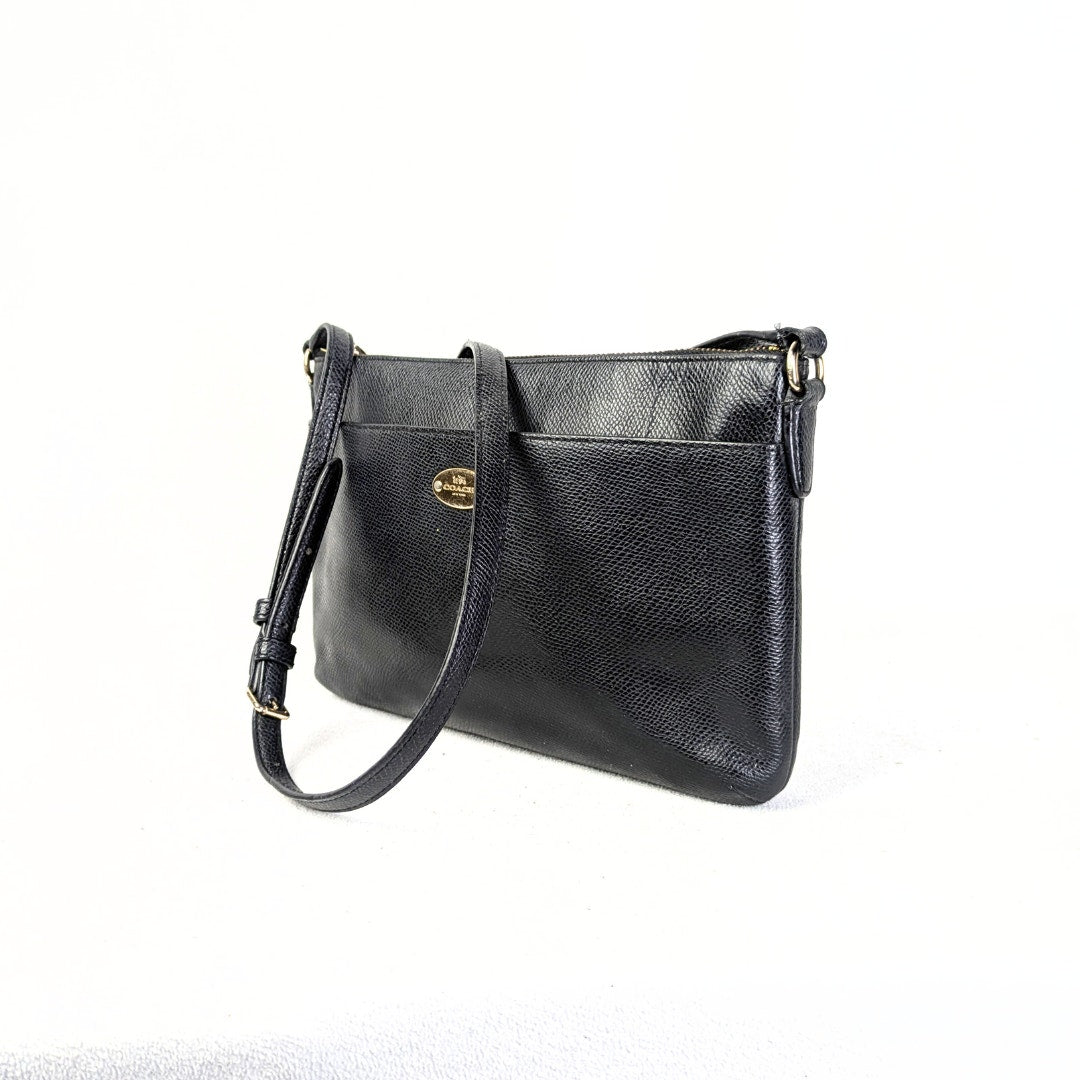 A black Coach Polly Crossgrain Leather Crossbody Bag with gold-tone hardware, an adjustable leather strap, and a front slide pocket.