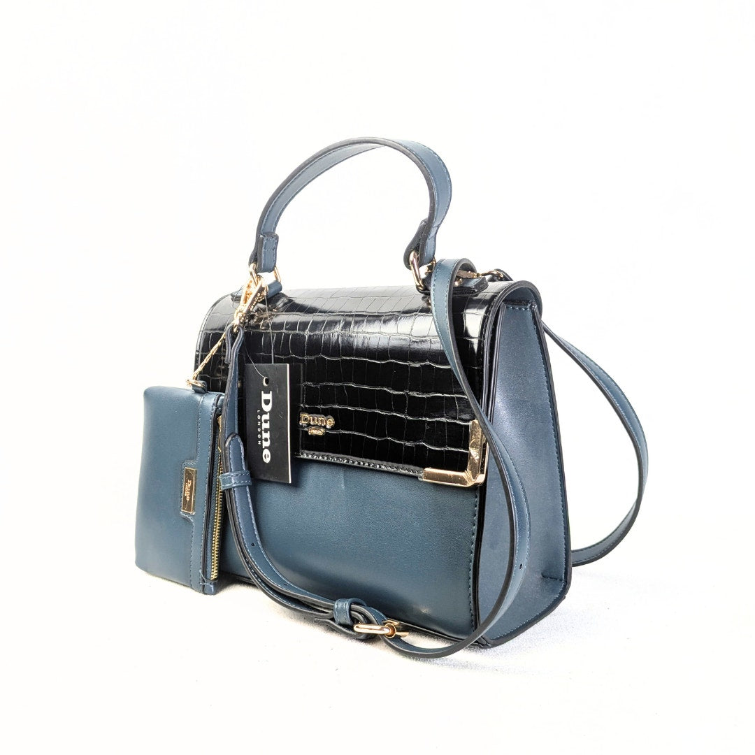 A navy blue Dune London satchel handbag with a convertible crossbody strap, featuring a black patent leather flap, gold-tone hardware, and a matching wallet.