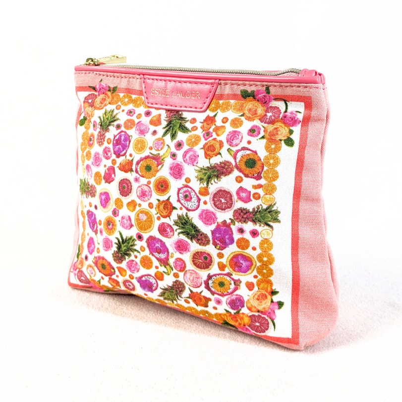 A pink Estée Lauder makeup bag with a small citrus fruits print and gold hardware on a white background.