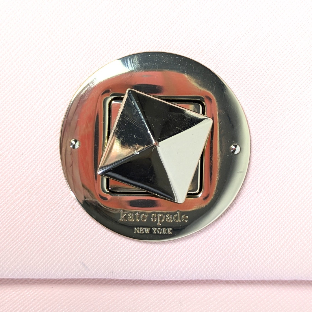 The close-up on the hardware lock of the Kate Spade New York Newbury Lane Sally Crossbody Bag in Blush Pink.