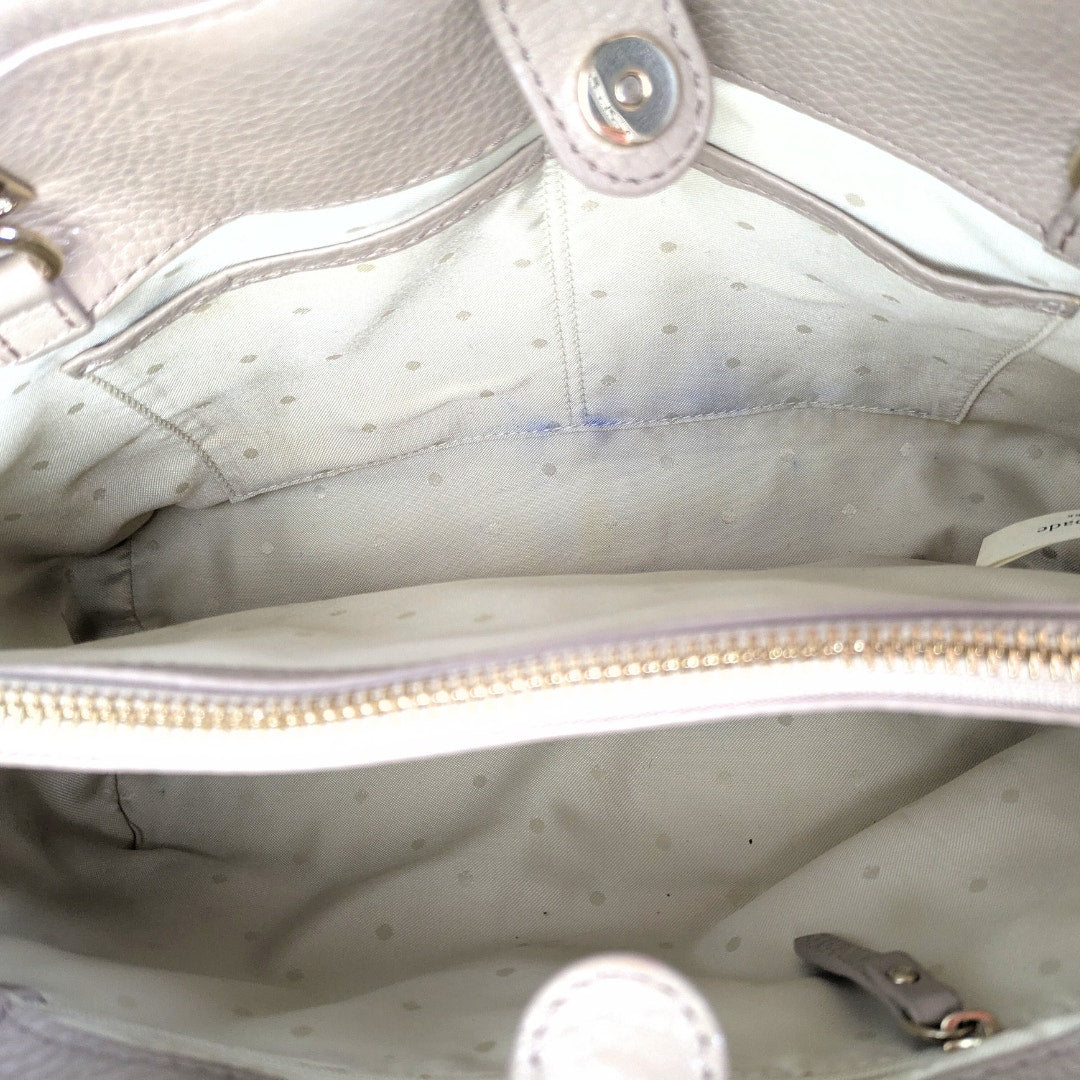 Close-up of a light-colored handbag with a zipper, showing texture and stitching details.
