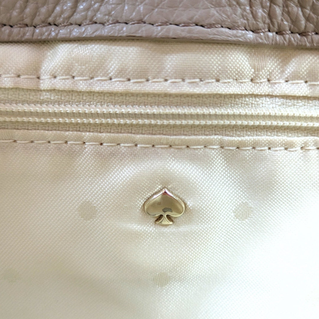 Close-up of a beige handbag with a gold logo on a beige background
