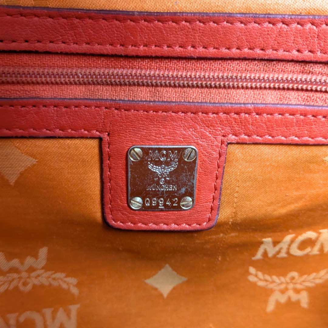 The internal metal logo plaque of the MCM Monogram Embossed Leather Satchel Shoulder Bag.