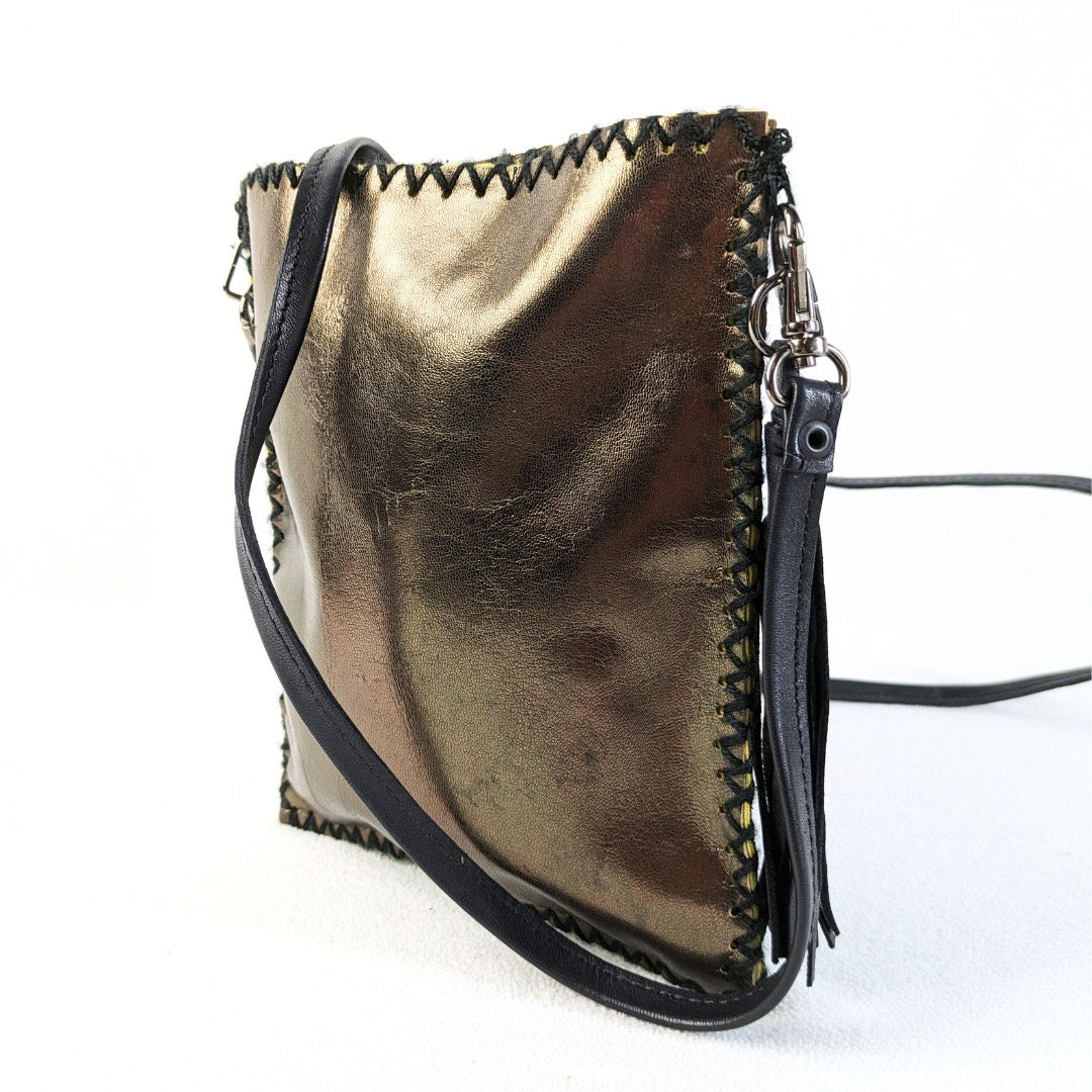 A metallic gold faux leather crossbody bag with a black leather strap and a black zipper, featuring a yellow canvas interior and a decorative tassel.