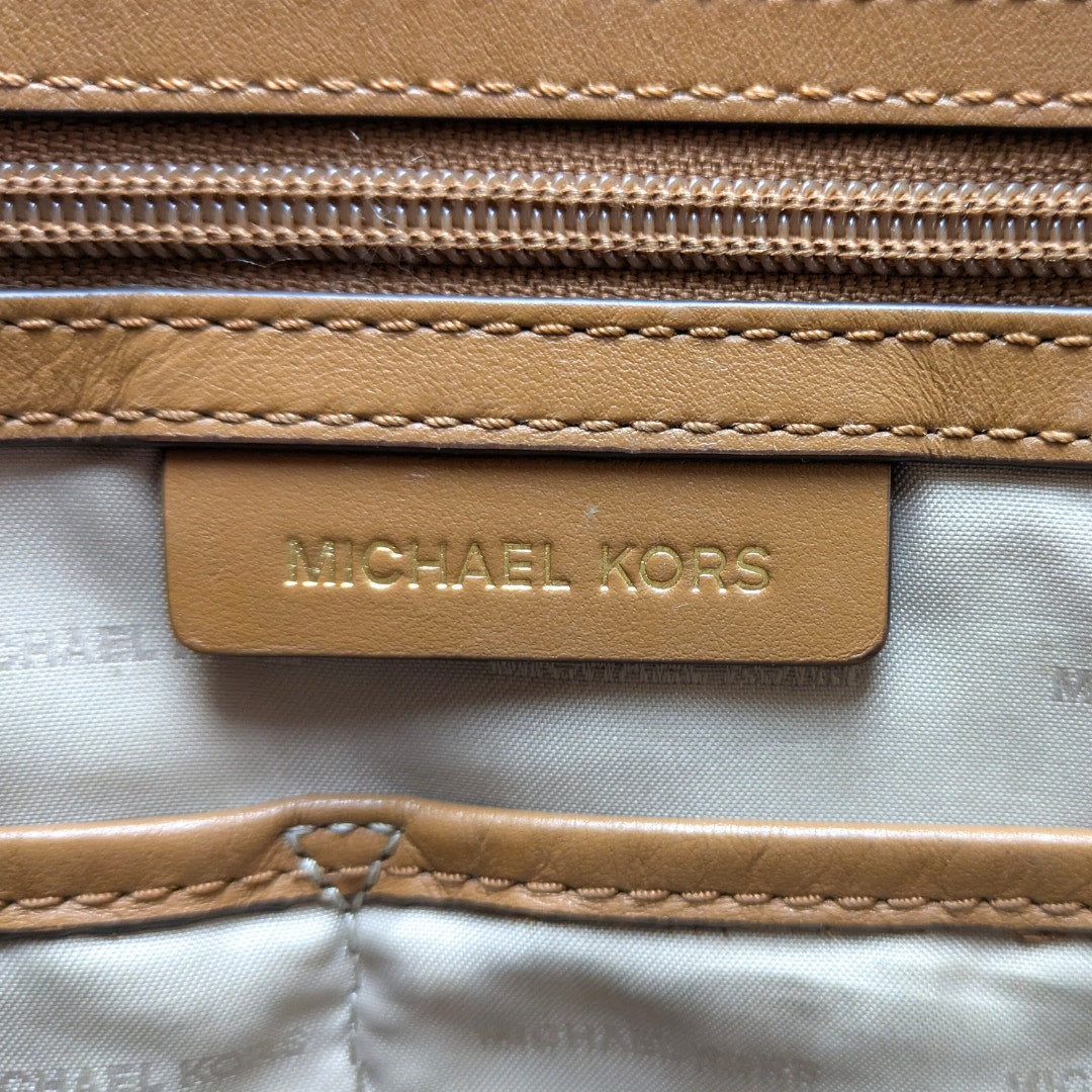 The close-up view of the leather embossed logo patch for the Michael Kors Signature Raven Large North South Top Zip Tote.