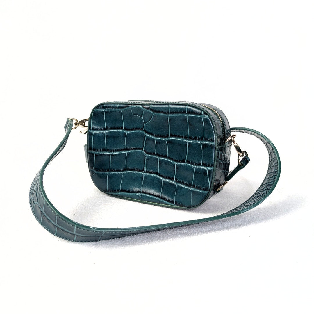 A crocodile embossed leather crossbody bag with a green exterior, gold-tone hardware, and a pink canvas lining.