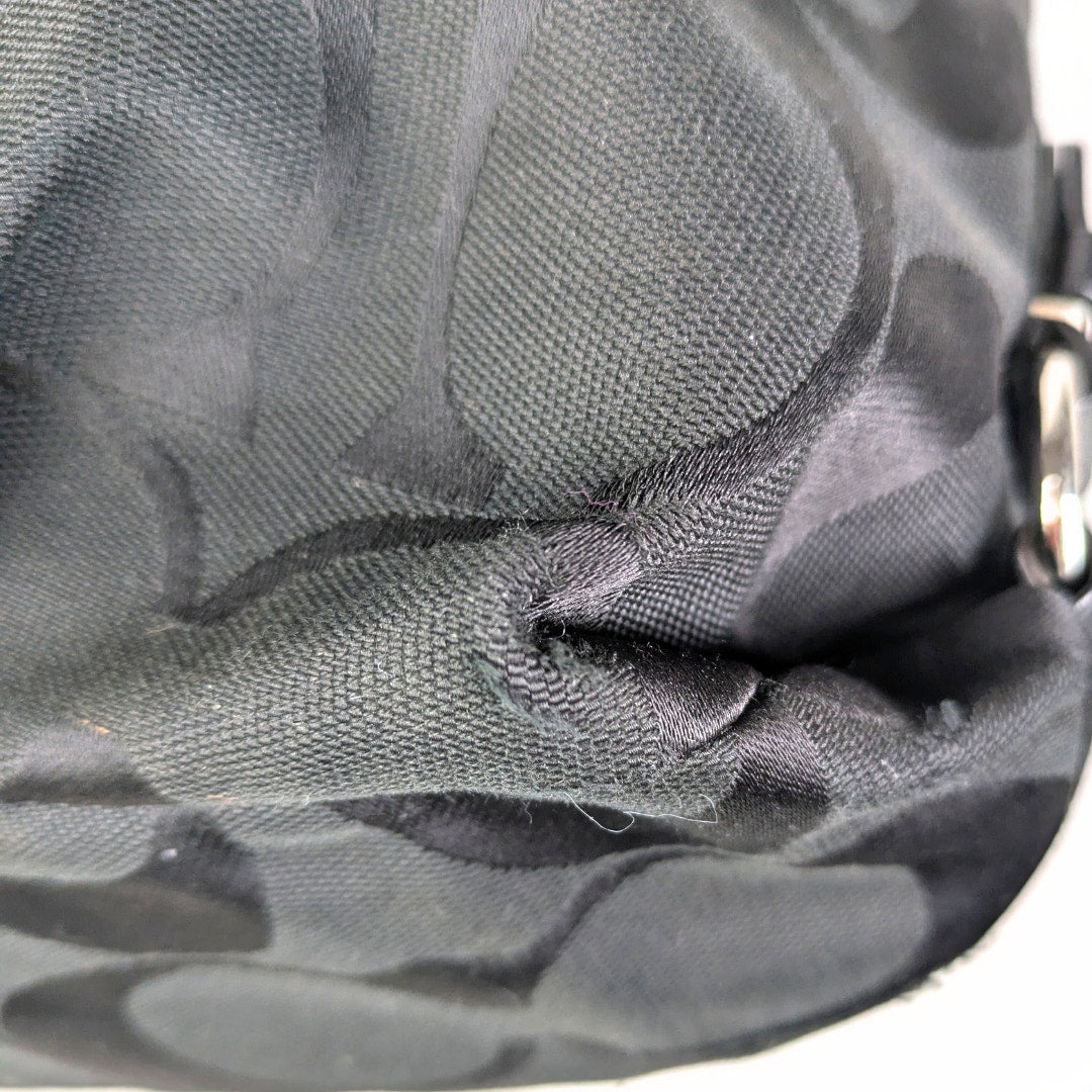 The close-up on the bottom corner of the Coach Monogram Hobo Shoulder Bag, captured on the white background. 