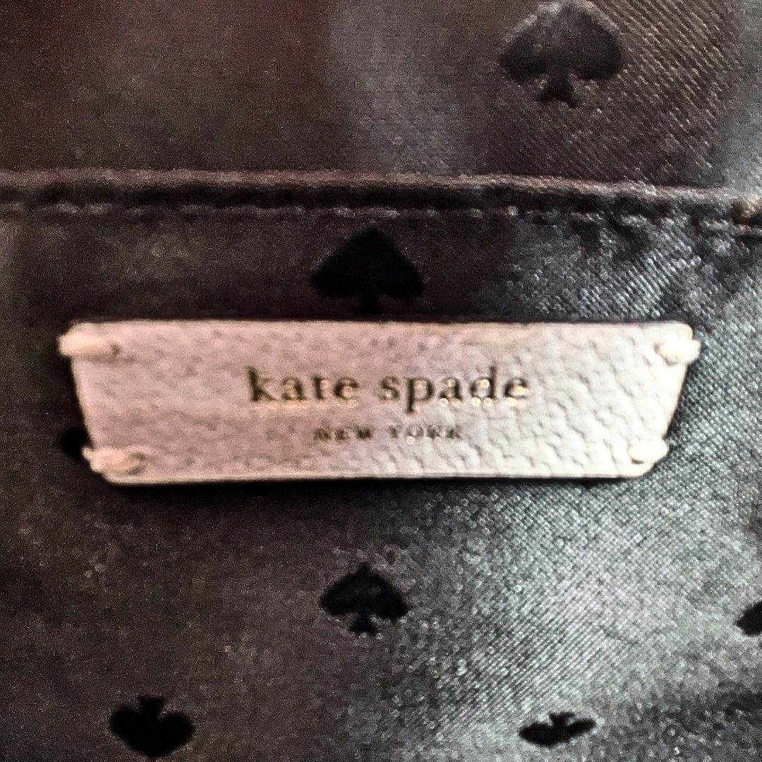 Close-up of a Kate Spade New York label on a dark fabric background with spade patterns.