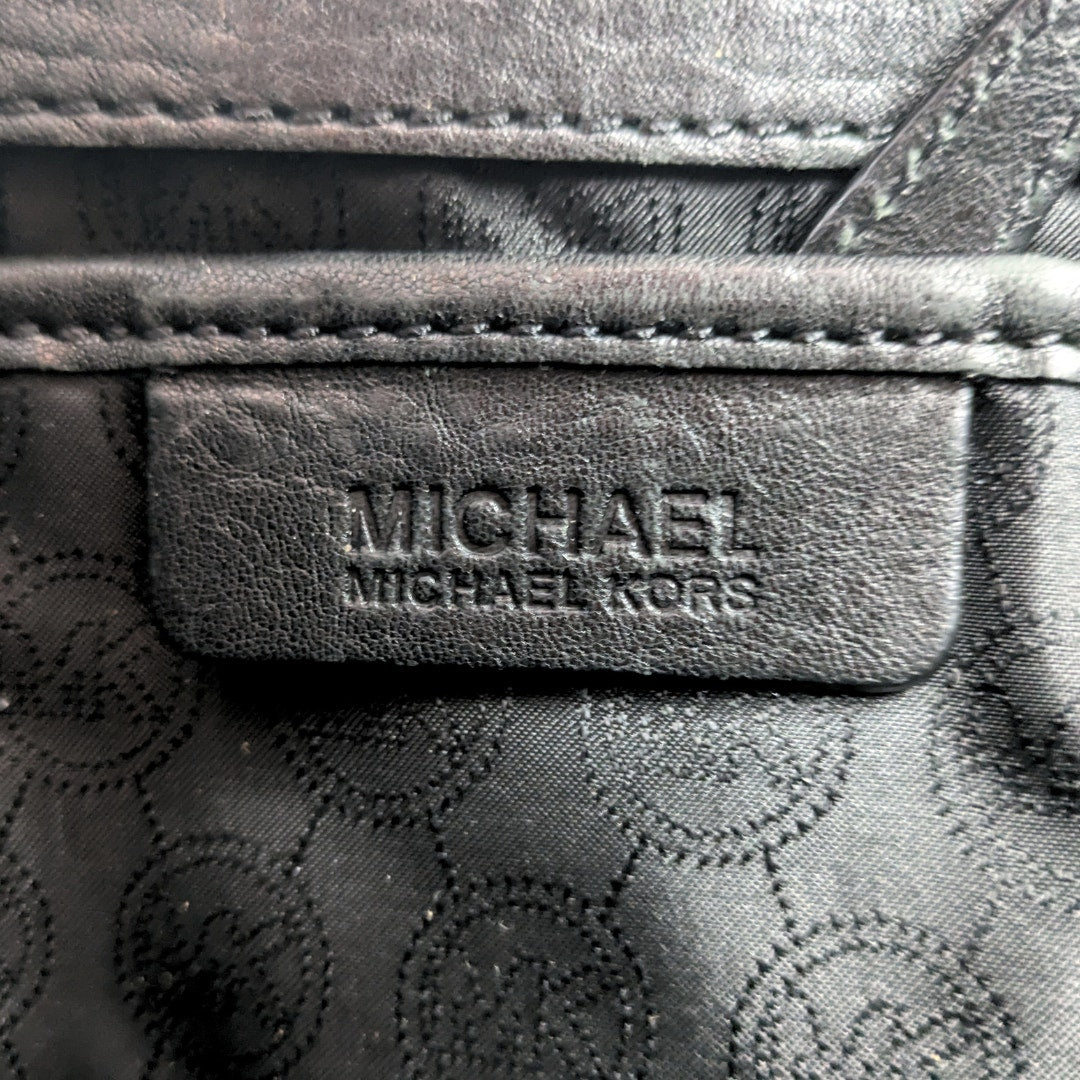 Close-up of a Michael Kors logo on a black leather product with a patterned background.