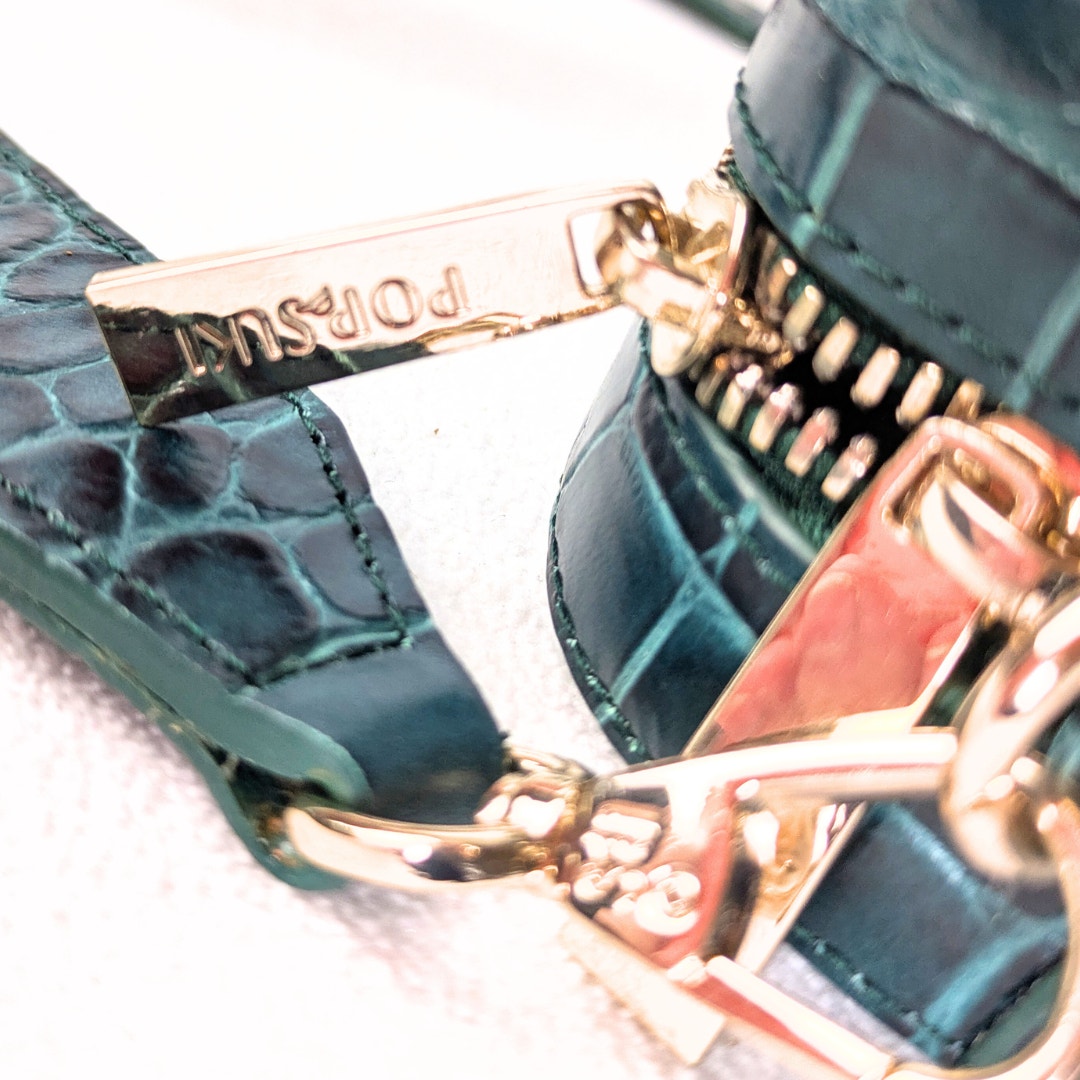 The gold-tone hardware of the Emerald Pop & Suki Crocodile Embossed Leather Camera Crossbody Bag.