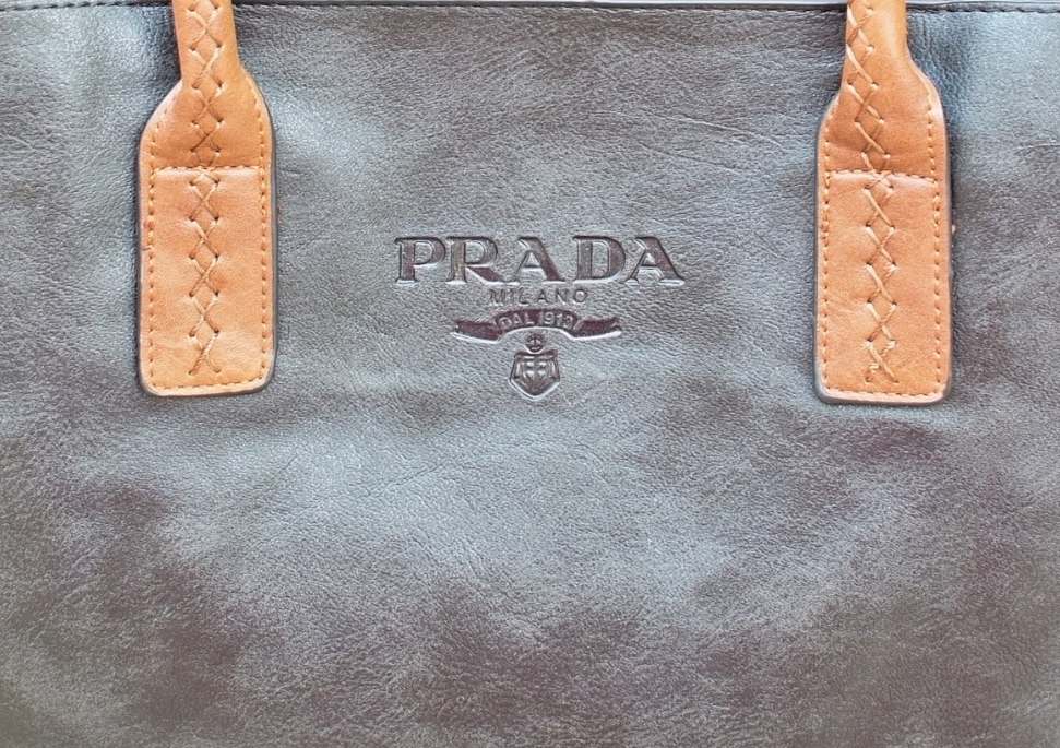 Front leather part of the brown Prada bag. It presents the embossed logo and camel handbag's handles.